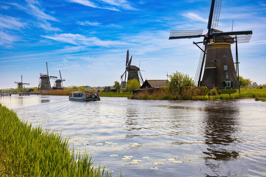 Perspective view of the canal in which five windmills and a tourist barge sailing through the canal can be seen on the shore. Kindedijk, Netherlands
