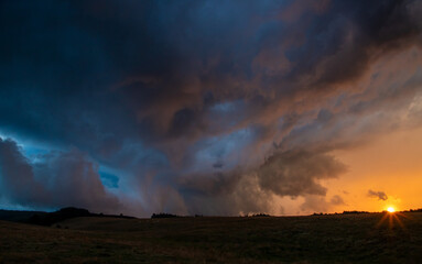 Naklejka na ściany i meble Landscape with a sunset on the field with storm clouds