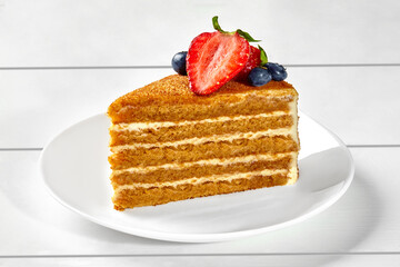 Slice of honey cake with cheese cream, caramel crumbs and berries