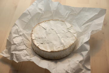 Unwrapped French Brie Cheese on a table next to a kitchen window at sunset