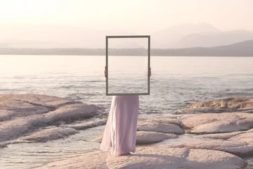 Foto op Plexiglas woman holding a frame that surreally reflects the landscape , abstract concept © Cristina Conti