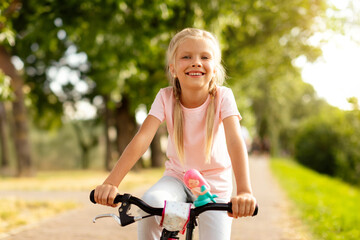 Portrait of happy cute girl enjoy riding bike in city park on road, looking and smiling at camera