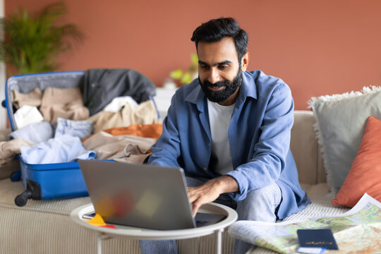 Happy Indian Traveler Guy Websurfing On Laptop In Living Room