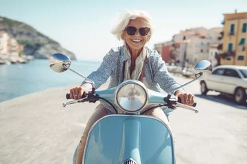 Photo sur Plexiglas Scooter Cheerful senior woman riding blue scooter in Italy, retired granny enjoying summer vacation, trendy bike road trip