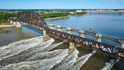 Fototapeta premium Truss arch bridge over large dam blue river water and white water rapids aerial of distant shore