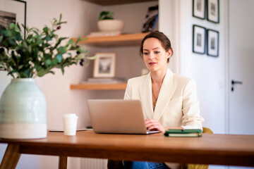 Fototapeta na wymiar Confident young woman sitting at table and using laptop for work at home
