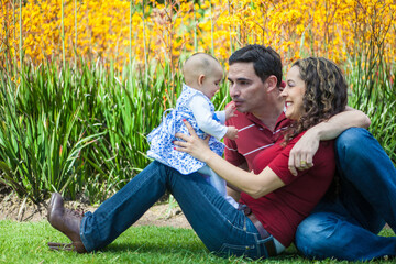 Naklejka na ściany i meble Young parents having fun outdoors with their six months old baby girl. Happiness concept. Family concept