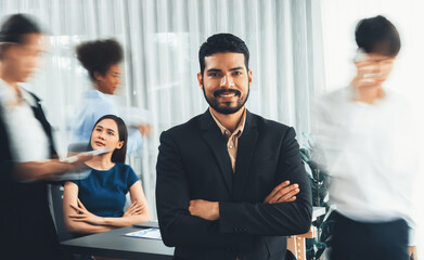Businessman portrait poses confidently with diverse coworkers in busy meeting room in motion...