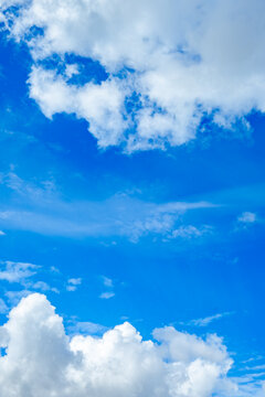 Cloudscape. Blue sky with white cumulus clouds in the noon. Vertical cloudy wallpaper. Natural background. Up view. Beauty in nature. Copy space