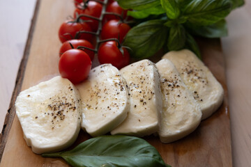 Fresh mozzarella, tomatoes, and sweet Italian basil on a wood cutting board next to a kitchen window at sunset 