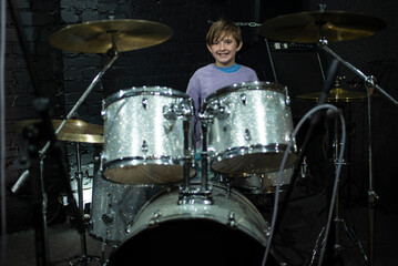Fototapeta na wymiar A 10 year old boy sits behind a silver drum kit. happy child learns to play the drums.