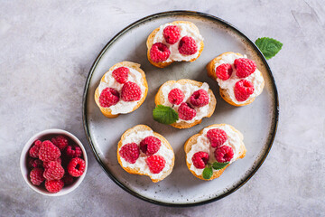 Close up of appetizing crostini with ricotta, raspberries and mint on a plate on the table top view