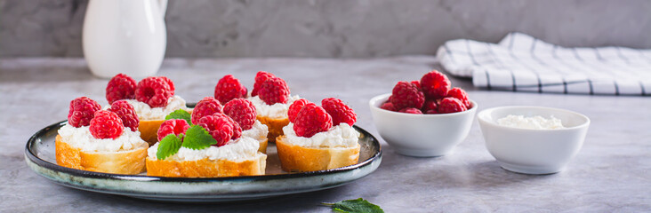 Fresh crostini with ricotta, raspberries and mint on a plate on the table web banner