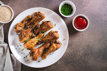 Spicy baked chicken drumsticks with green onions and sesame seeds on a plate top view