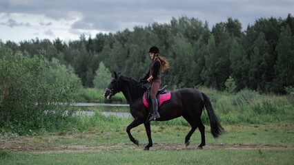 Equestrian sports. A young woman in the saddle, a rider and her horse outdoors, riding in the woods.