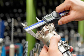 The worker operator of the cnc machine tool measures the cutting tool with a caliper for further work on milling and turning machines.