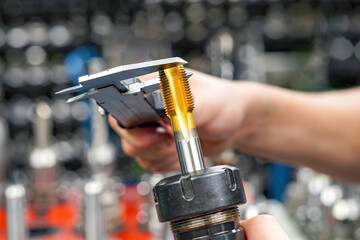 Measuring a cutting tool with a caliper for a CNC machine tool.
