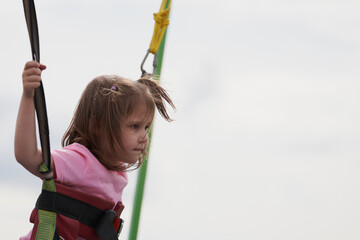 Portrait of a little girl in the air bouncing on a bungee trampoline.