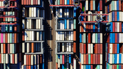 Rows of cargo containers rest atop massive container ships docked at an industrial port. Aerial...