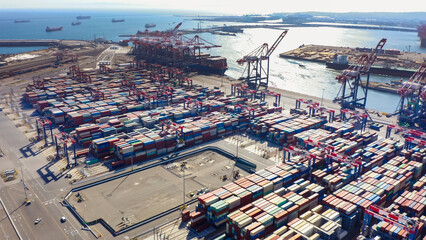 Rows of cargo containers rest atop massive container ships docked at an industrial port. Aerial view cargo ship terminal. Aerial view of shipping container port terminal. 