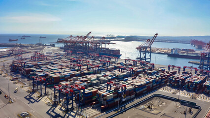Rows of cargo containers rest atop massive container ships docked at an industrial port. Aerial...
