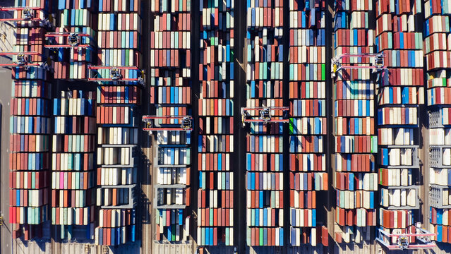 Rows of cargo containers rest atop massive container ships docked at an industrial port. Aerial view cargo ship terminal. Aerial view of shipping container port terminal. 