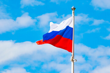 flag of the Russian Federation on a flagpole. Blue clear sky with clouds.