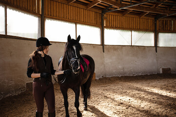 Equestrian sports. A young woman in a sports uniform, a rider and her horse in the arena, preparing...