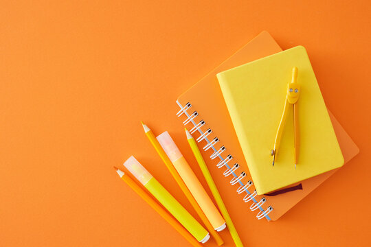 School preparation theme. Top view composition of notebooks, pencils, colorful markers, compass on orange background with empty space for promo or text