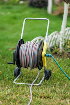 garden hose on a reel on wheels for watering plants stands in the garden.