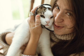 Woman in cozy knitted sweater hugging cute little cat after veterinary. Stylish female cuddling...