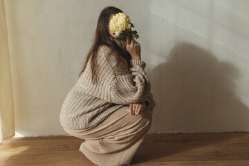 Stylish woman in cozy knitted sweater posing with chrysanthemum flower on background of rural...