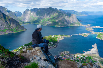 Relaxed happy hiker enjoys stunning views on Reinebringen peaks of Lofoten islands, fjords, Norway....