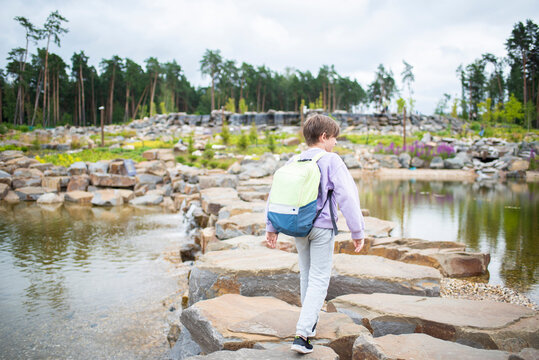 The boy walks along the bridge of stones, past the pond, walks in the Malevich park. .