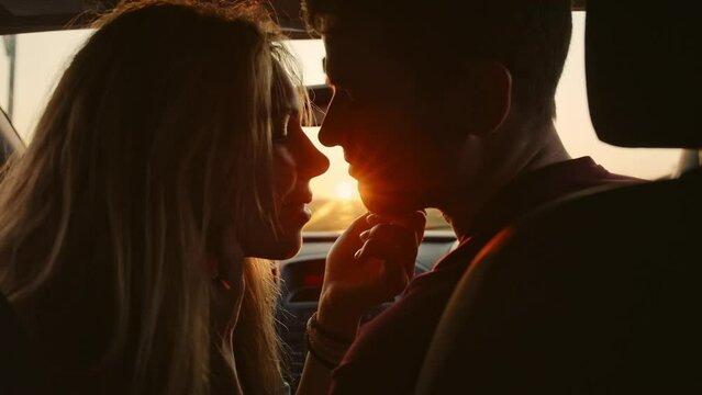 Portrait of young casual pretty lovers looking at each other with tenderness and sitting in car at sunset while long roadtrip. Moment before a romantic kiss. Concept of love and travelling