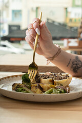 Close up of a fork in a woman's hand over a plate with delicious food in a restaurant