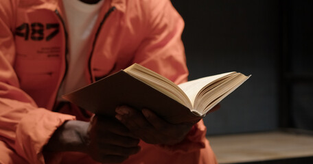 African American man in orange prison uniform reads Bible while sitting in cell