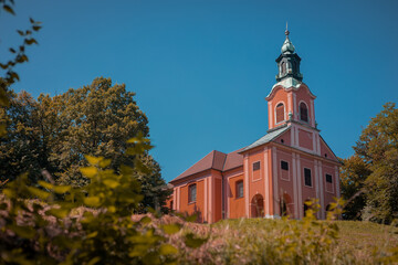 Red church on Rozik hill above Ljubljana surrounded by lush green trees and grassy meadows....