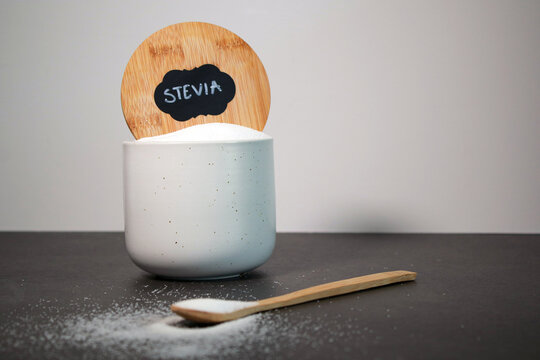 Natural stevia sweetener in a white bowl with a wooden spoon, grey marble table