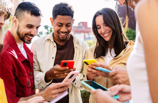 Happy Group Of Young Student Friends Holding Mobile Phones At City Street. Diverse Millennial People Using Cell Phones Addicted To Social Media App. Technology And Youth Concept.