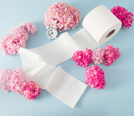 Toilet paper roll with pink fresh flowers and white clock against pastel blue background. top view hygiene concept