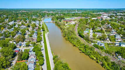 Suburban houses next to large muddy river and winding train tracks aerial city