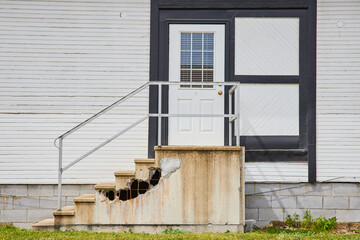 House with white siding and door with black frames and busted concrete stairs