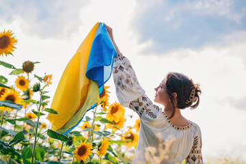 Young ukrainian woman waving national flag on sunflowers, wheat field background