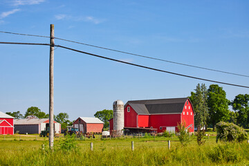 Red barn and green fields with tractors and a telephone pole with wires cutting through blue sky © Nicholas J. Klein