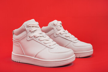 pair of white youth sneakers on red background close-up.