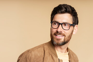 Obraz premium Portrait of smiling handsome bearded man wearing stylish eyeglasses looking away isolated on beige background, copy space. Vision concept 