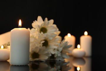 White chrysanthemum flowers and burning candles on black mirror surface in darkness, space for text. Funeral symbols - obrazy, fototapety, plakaty