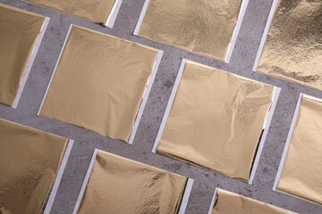 Fototapeta premium Many edible gold leaf sheets on grey textured table, flat lay