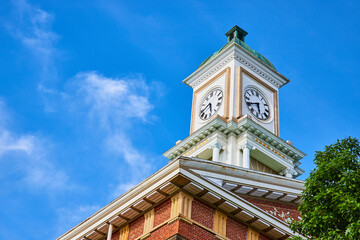 Fototapeta na wymiar Clock tower on brick building roof with blue skies and green tree top